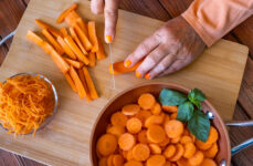 Close-up of an older adult cutting fresh carrots on a wooden cutting board