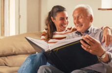 A older adult man and his daughter smiling while looking at a photo album together.